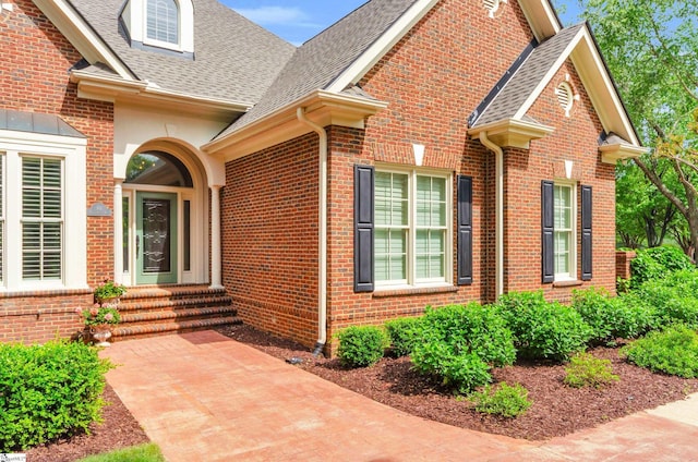 doorway to property featuring brick siding and a shingled roof