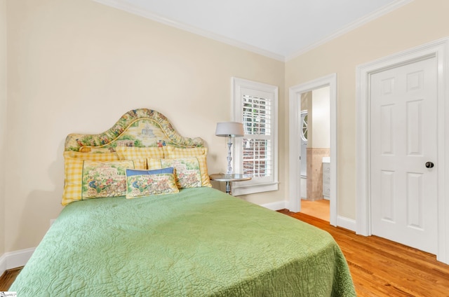 bedroom featuring crown molding, baseboards, wood finished floors, and ensuite bathroom