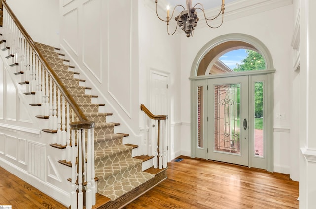 foyer entrance with an inviting chandelier, visible vents, stairs, wood finished floors, and a high ceiling