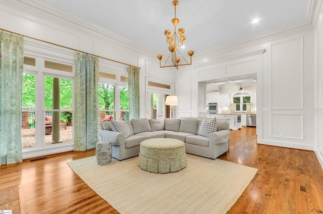 living area with visible vents, ornamental molding, a decorative wall, wood finished floors, and a chandelier