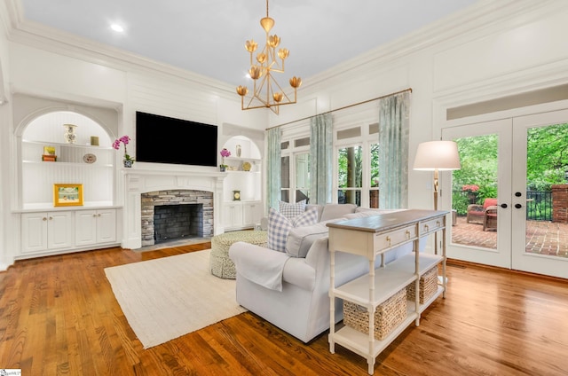 living area with crown molding, a chandelier, a stone fireplace, built in features, and french doors