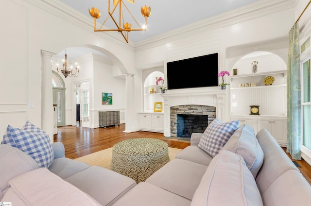 living room featuring a stone fireplace, built in shelves, wood finished floors, an inviting chandelier, and ornamental molding