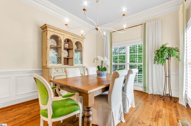 dining space featuring visible vents, ornamental molding, a wainscoted wall, a chandelier, and light wood finished floors