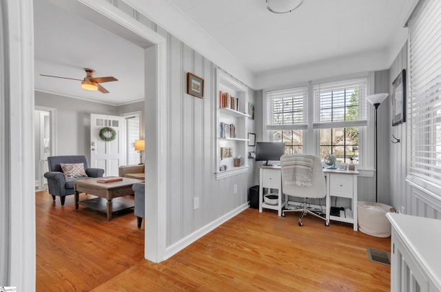 office space featuring a ceiling fan, visible vents, built in features, light wood-type flooring, and ornamental molding