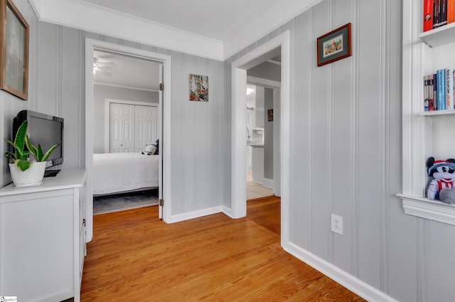 corridor with baseboards, ornamental molding, a decorative wall, and light wood finished floors