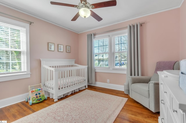 bedroom featuring crown molding, light wood-style floors, a nursery area, and multiple windows