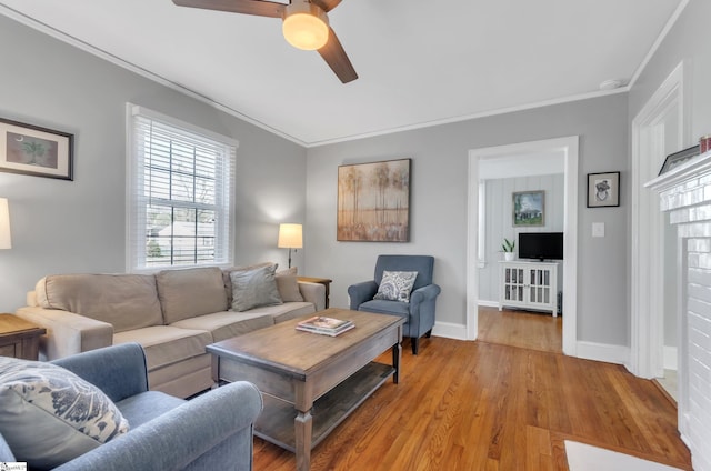living area featuring crown molding, baseboards, ceiling fan, and light wood-style flooring