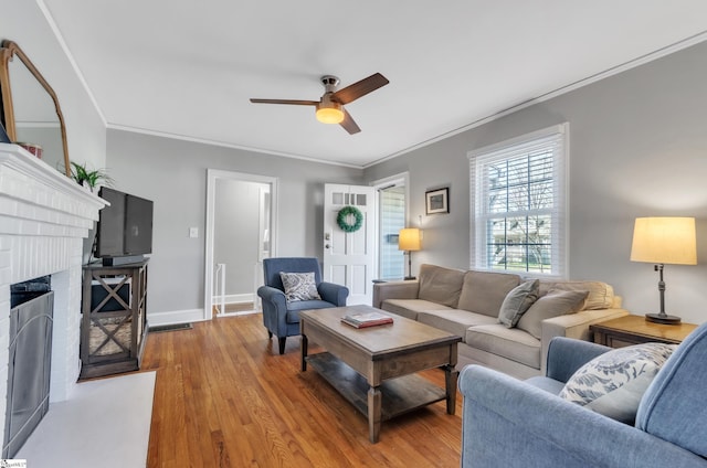 living area with a ceiling fan, a fireplace, wood finished floors, baseboards, and ornamental molding