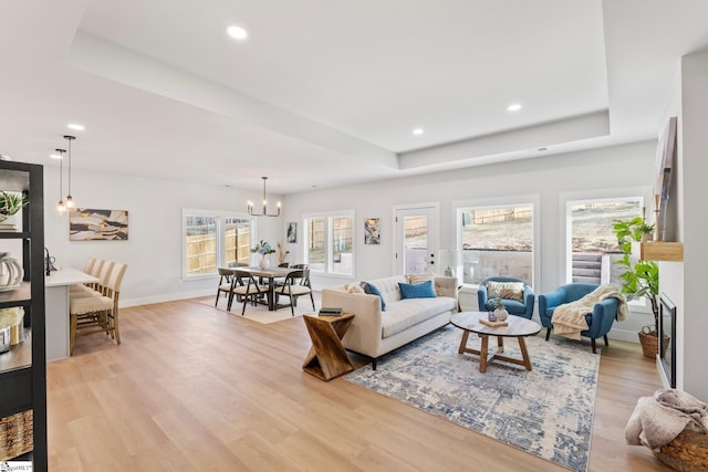 living room with a notable chandelier, recessed lighting, baseboards, light wood-type flooring, and a tray ceiling