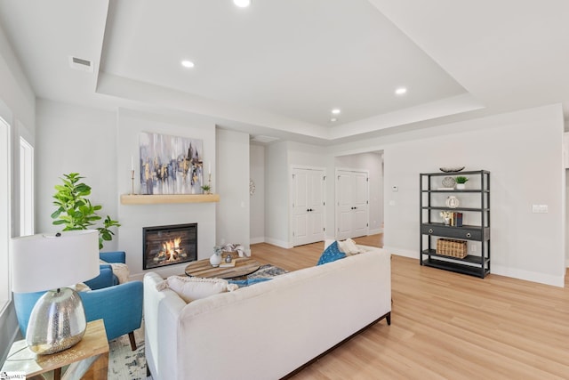 living room featuring visible vents, a glass covered fireplace, light wood-style floors, a tray ceiling, and recessed lighting