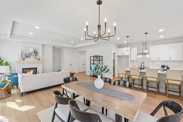 dining room featuring a raised ceiling, recessed lighting, a notable chandelier, and light wood finished floors
