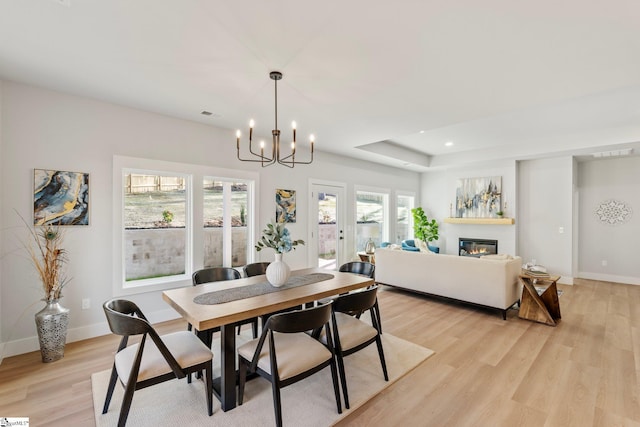dining area featuring baseboards, light wood-style flooring, a glass covered fireplace, and a notable chandelier