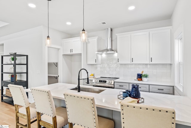 kitchen featuring wall chimney range hood, tasteful backsplash, a sink, electric stove, and a kitchen bar