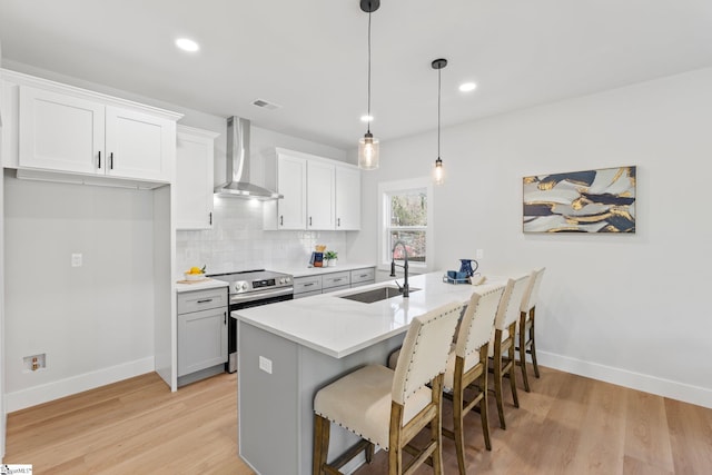 kitchen featuring baseboards, a sink, stainless steel range with electric cooktop, and wall chimney range hood