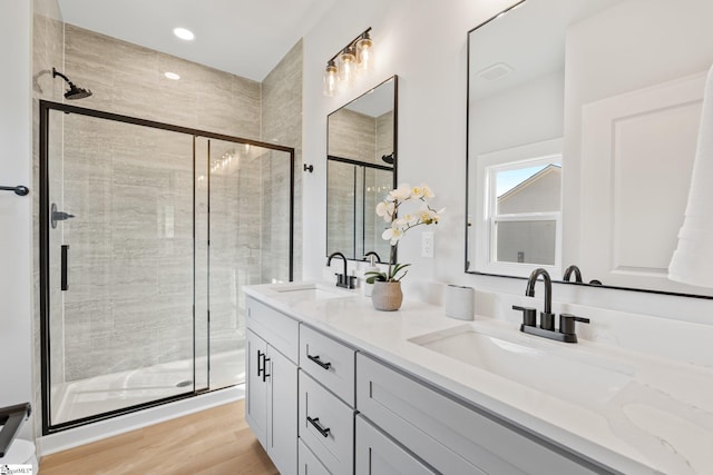 full bathroom featuring wood finished floors, a sink, a stall shower, and double vanity