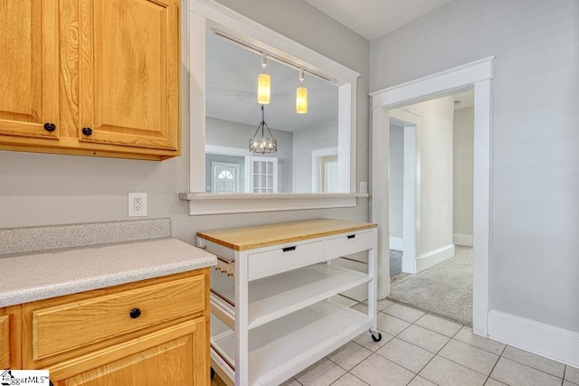 kitchen featuring light colored carpet, light countertops, a chandelier, baseboards, and light tile patterned floors