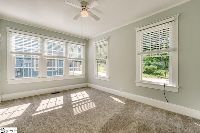 carpeted empty room featuring baseboards, ornamental molding, ceiling fan, and visible vents