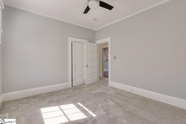 empty room with carpet floors, ceiling fan, ornamental molding, and baseboards