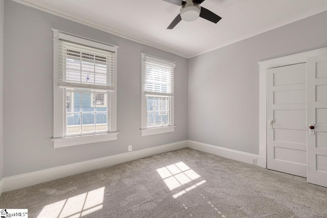 carpeted spare room featuring crown molding, ceiling fan, and baseboards