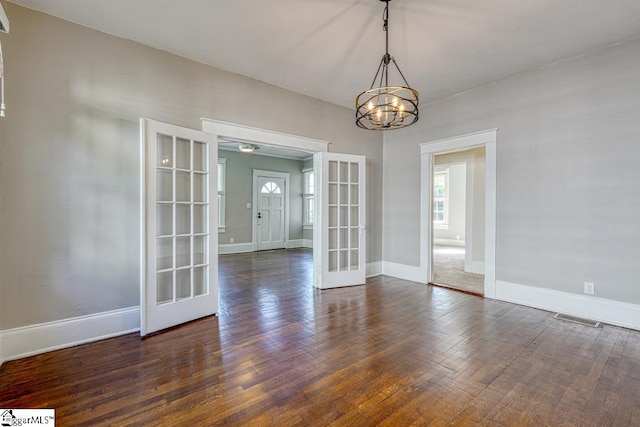 spare room featuring french doors, dark wood-style flooring, visible vents, baseboards, and a chandelier
