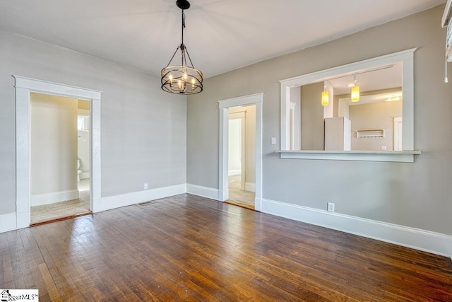 spare room featuring wood-type flooring, baseboards, and a notable chandelier