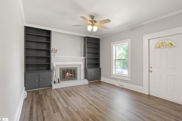 unfurnished living room featuring crown molding, a brick fireplace, a ceiling fan, wood finished floors, and visible vents