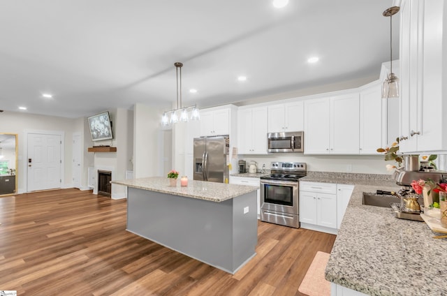 kitchen with appliances with stainless steel finishes, a center island, a fireplace, white cabinets, and light wood-style flooring