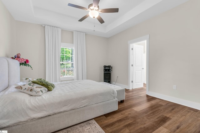 bedroom with baseboards, a raised ceiling, ceiling fan, and wood finished floors