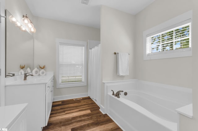 bathroom with a bath, visible vents, wood finished floors, vanity, and baseboards