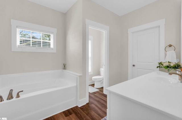 bathroom featuring vanity, wood finished floors, toilet, baseboards, and a bath