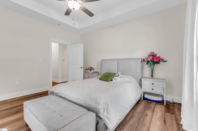 bedroom with a ceiling fan, baseboards, wood finished floors, and a raised ceiling