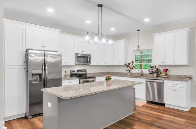 kitchen with white cabinets, appliances with stainless steel finishes, a center island, recessed lighting, and wood finished floors