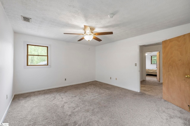 carpeted spare room featuring baseboards, a ceiling fan, a textured ceiling, and visible vents