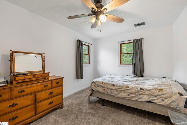 carpeted bedroom featuring a textured ceiling, visible vents, multiple windows, and ceiling fan