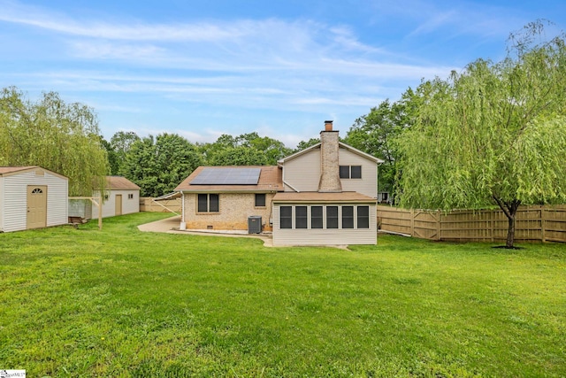 rear view of property with a chimney, a sunroom, roof mounted solar panels, a storage shed, and an outbuilding
