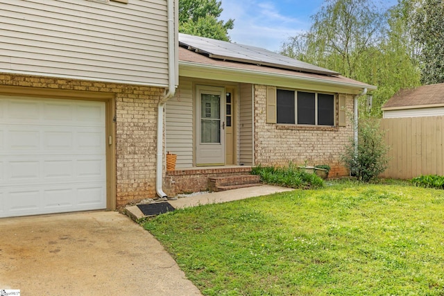 view of exterior entry featuring fence, brick siding, solar panels, a yard, and driveway