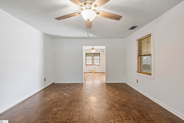 empty room featuring a textured ceiling, ceiling fan, visible vents, and baseboards