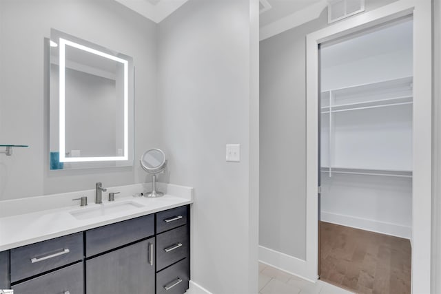 bathroom featuring vanity, baseboards, a walk in closet, and visible vents