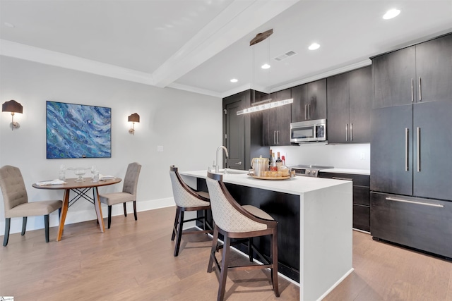 kitchen with light countertops, baseboards, a breakfast bar, stainless steel appliances, and an island with sink