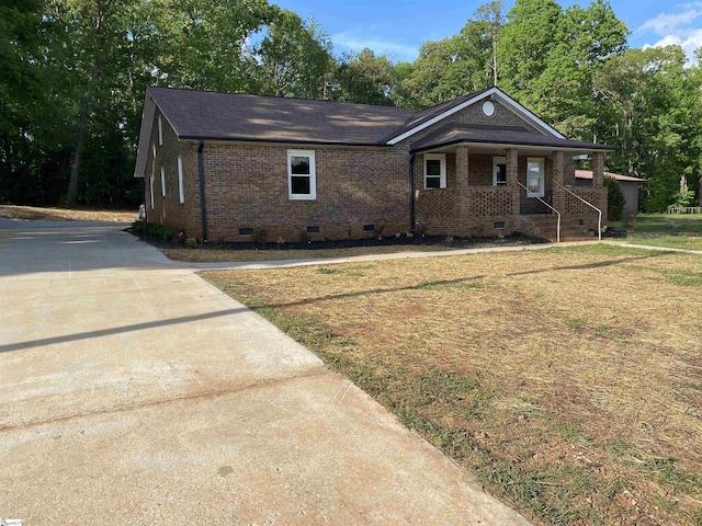 view of front of property with a shingled roof, brick siding, a front yard, crawl space, and covered porch