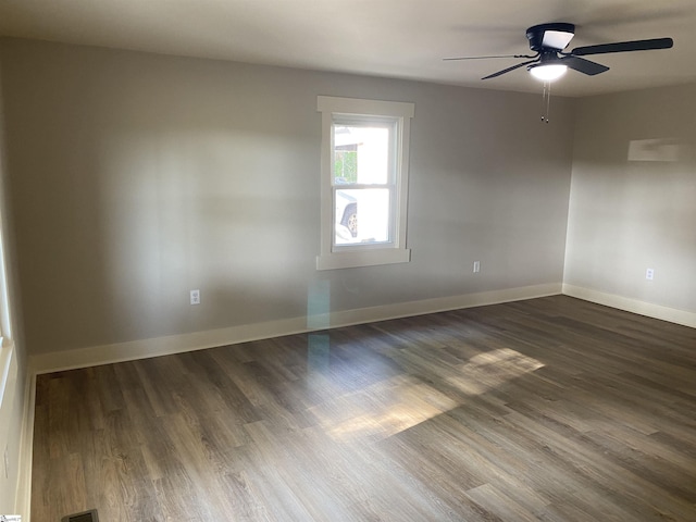 spare room featuring baseboards, ceiling fan, and dark wood-type flooring