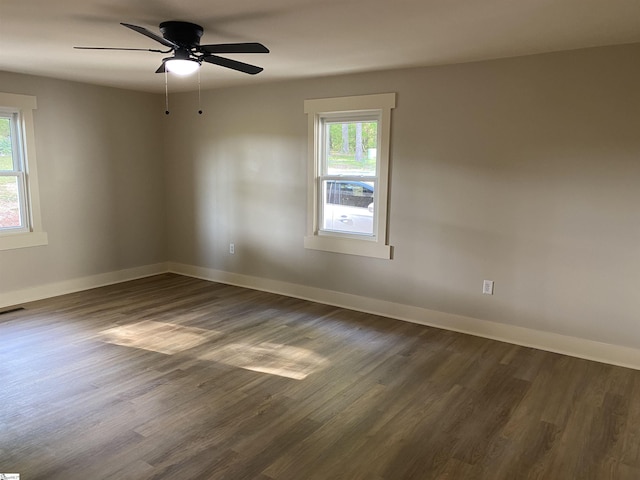 spare room featuring dark wood-type flooring, a ceiling fan, baseboards, and a wealth of natural light