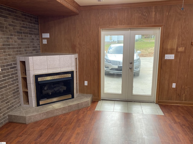 unfurnished living room with a tiled fireplace, french doors, wood walls, and wood finished floors
