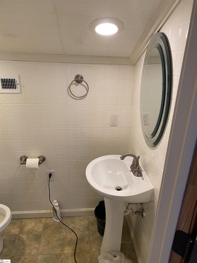 bathroom with visible vents, a sink, and tile walls