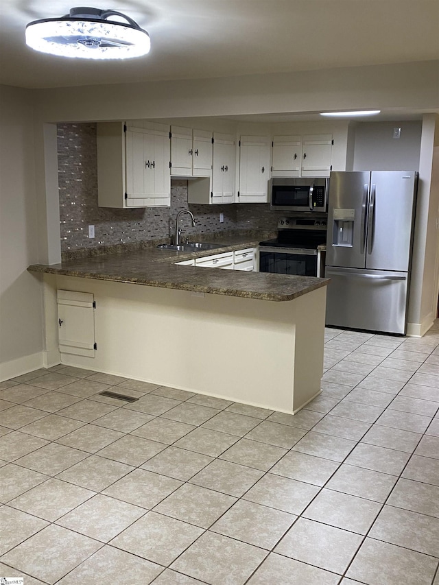 kitchen featuring tasteful backsplash, a sink, a peninsula, stainless steel appliances, and light tile patterned flooring