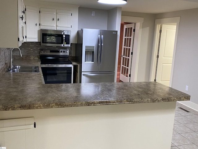kitchen featuring light tile patterned flooring, dark countertops, a sink, stainless steel appliances, and a peninsula