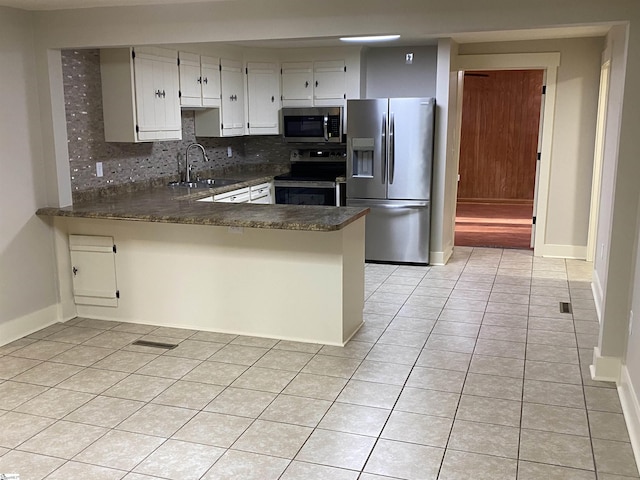 kitchen with decorative backsplash, dark countertops, a sink, appliances with stainless steel finishes, and light tile patterned floors