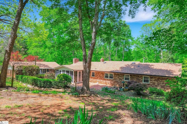 rear view of property featuring brick siding, a chimney, and a sunroom
