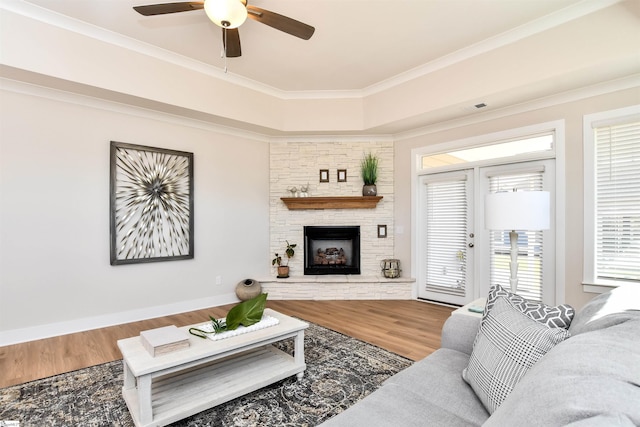living area with crown molding, a stone fireplace, a ceiling fan, wood finished floors, and visible vents