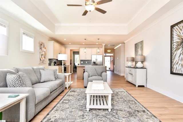 living room with crown molding, ceiling fan, a tray ceiling, and light wood-style floors